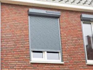 Vooraanzicht van een woning, inzoomend op de bovenverdieping waar we een raamkozijn met rolluik zien.